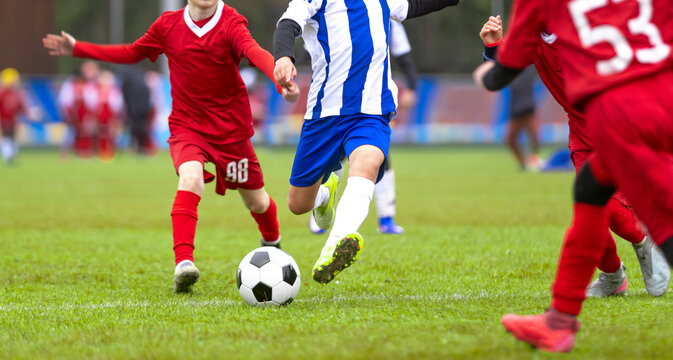 Junior Soccer Player in Blue and White Striped Kit Dribbling Ball Past Defenders in Red Jerseys - Competitive Youth Football League Match Action