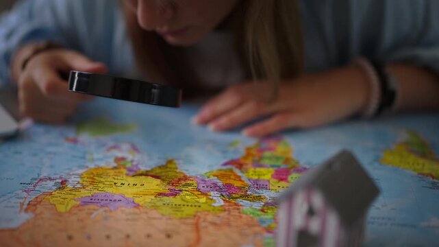 Curious woman with magnifying glass exploring world map for vacation destination, planning international travel adventure, choosing country for real estate investment or emigration