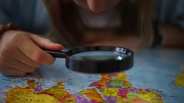 Curious woman with magnifying glass exploring world map for vacation destination, planning international travel adventure, choosing country for real estate investment or emigration