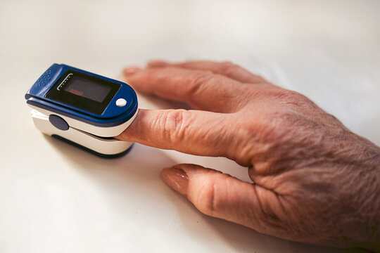 Close-up of a human hand using a pulse oximeter device to measure blood oxygen levels, with a white background highlighting the medical equipment