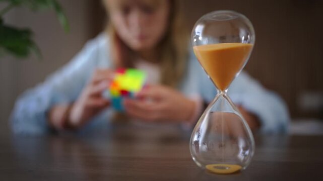 Hourglass counting down with young girl solving a challenging puzzle in blurred background, symbolizing problem solving, logical thinking, concentration and mental skills