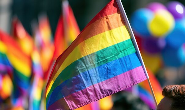 Rainbow flags wave during a pride parade in a city park filled with people celebrating diversity and equality