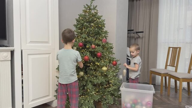 Children decorate Christmas tree at home placing ornaments and preparing for holiday. Family moment and festive atmosphere. Ideal for parenting, lifestyle and holiday campaigns.