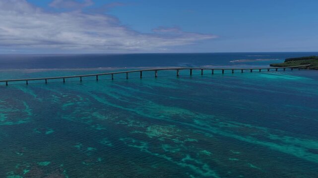 Horizontal cameo shot moving backward and upward over Kurima Bridge and turquoise coastal waters near the fishing port of Miyako, Okinawa, Japan
