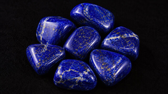 Polished lapis lazuli tumbled stone group macro showing deep ultramarine blue with gold pyrite sparkle flecks white calcite veins smooth waxy lustre on dark background