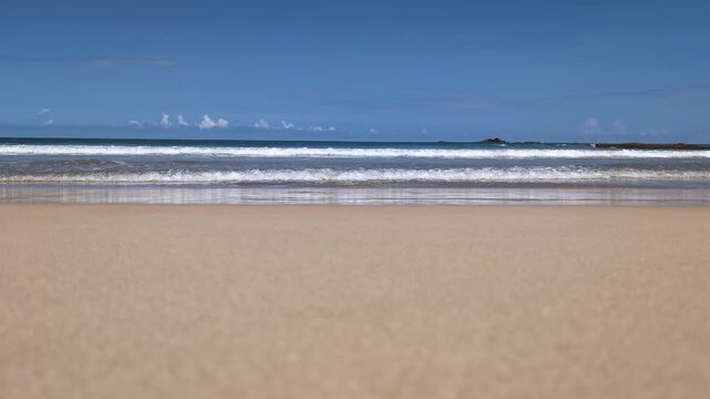 Beautiful 4K wide-angle footage of a vast sandy beach shoreline in Sri Lanka under a bright blue sky. Turquoise ocean waves gently roll and wash over the golden sand, leaving detailed white foam behin