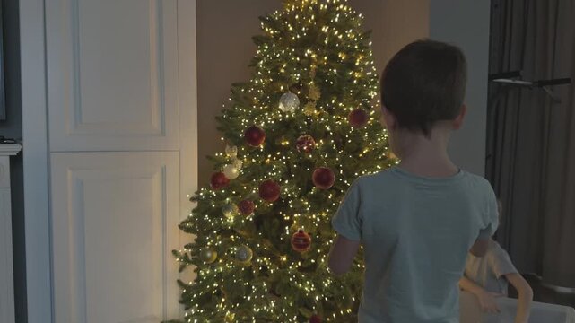 Children decorating Christmas tree in cozy evening setting. Warm lights and festive mood. Perfect for seasonal campaigns and family content.