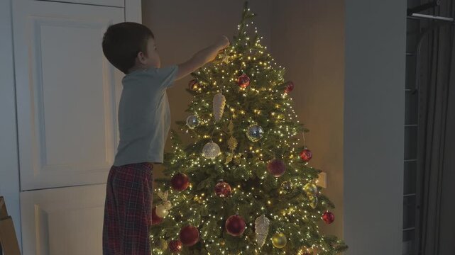 Close shot of child hanging ornament on Christmas tree. Simple festive moment. Suitable for family, holiday and lifestyle content.