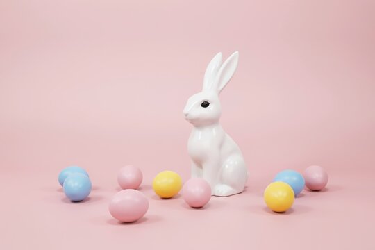 White ceramic easter bunny figurine surrounded by colorful pastel eggs on a pink background