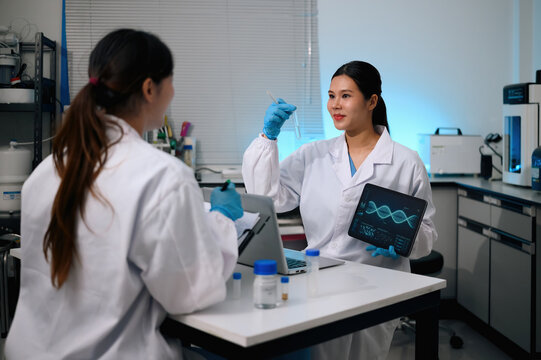 Two Asian Female Scientists Collaborating in Laboratory with DNA Data on Tablet and Test Tube