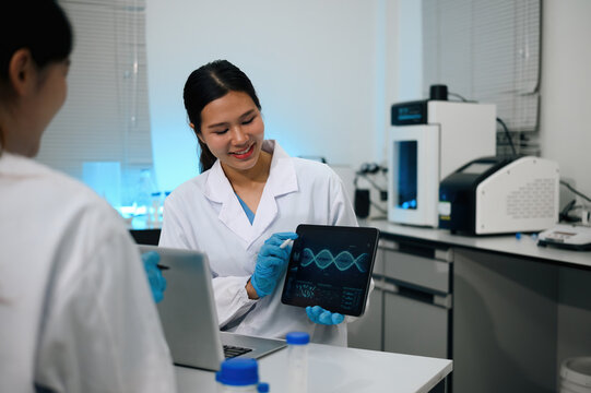 Asian Female Scientist Presenting DNA Data on Digital Tablet to Colleague in Modern Laboratory