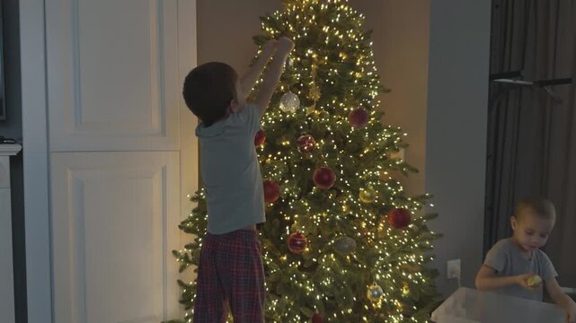 Two children decorating Christmas tree together placing ornaments and sharing festive moment. Ideal for family branding and holiday storytelling. 