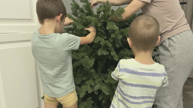 Mother and two children assembling artificial Christmas tree from sections. Family teamwork and festive preparation moment.