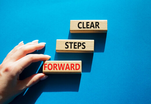 Clear steps forward symbol. Concept words clear steps forward on wooden blocks arranged as steps. Businessman hand arranging wooden blocks. Progress and planning concept. Blue background. Copy space.