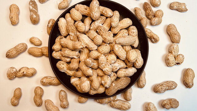 Bright flat lay unshelled peanuts piled on black plate against white surface