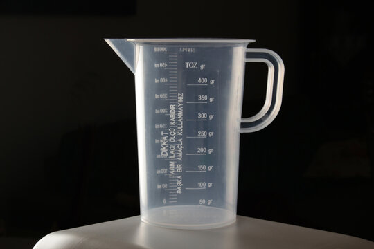 Transparent pesticide measuring cup on a black background.