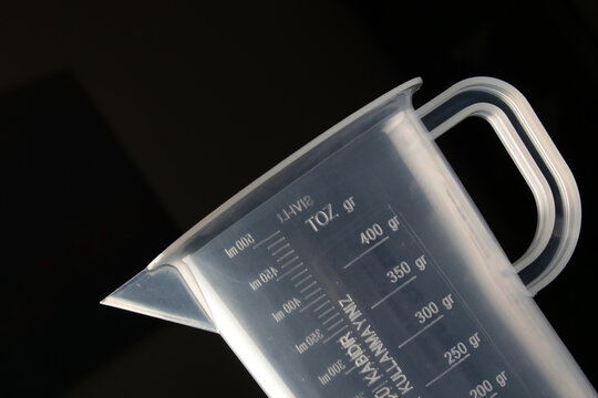 Transparent pesticide measuring cup on a black background.