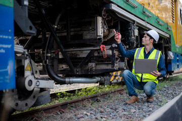 Male Railway Technician Inspecting Train Mechanical Parts Using Laptop and Tools © Wasana