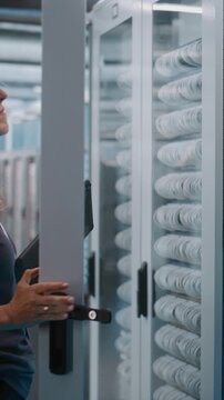 Professional Female IT Engineer Operates Digital Tablet and Open With Keys Server Rack. Mobile Diagnostics, Physical Security, and Infrastructure Monitoring Ensure Data Integrity. Vertical Shot.