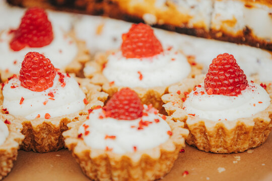 Miniature raspberry tarts with whipped cream and red sprinkles arranged on a brown surface, showcasing a delicious dessert presentation for culinary enthusiasts