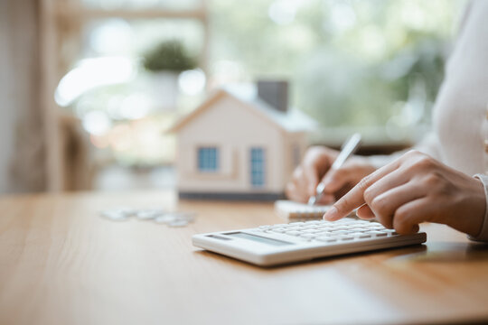 Real estate buyers balance a mortgage and savings for an asset in a budget as hands jot notes beside a toy building, fitting real estate and a mortgage to savings for an asset under a written budget.