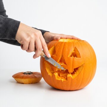 Hands carving a jack-o'-lantern with a knife on a white background