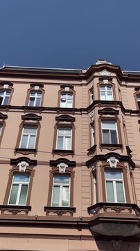 upward camera pan across multistory historic building exposing central projecting bay, rooftop cornice, and rows of white-framed sash windows with dark brown, with