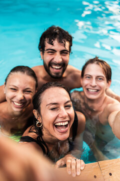 A group of four friends laughs joyfully while taking a selfie in a refreshing pool, capturing the essence of a carefree summer day. The vibrant blue water enhances the cheerful mood.