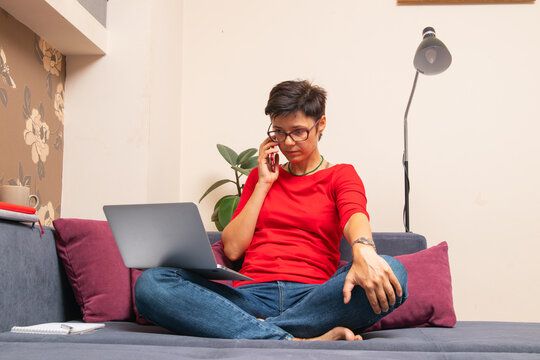 Woman talking on phone while sitting on couch with laptop in modern living room