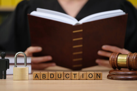 A judge in a dark robe is engrossed in reading a large book about abduction cases.
