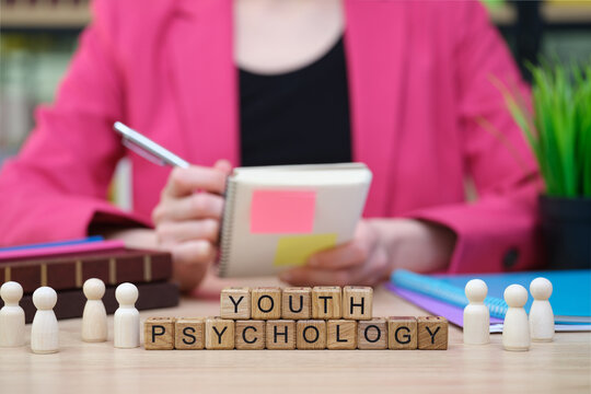 A professional seated at a desk holds a notebook, pondering ideas on youth psychology.