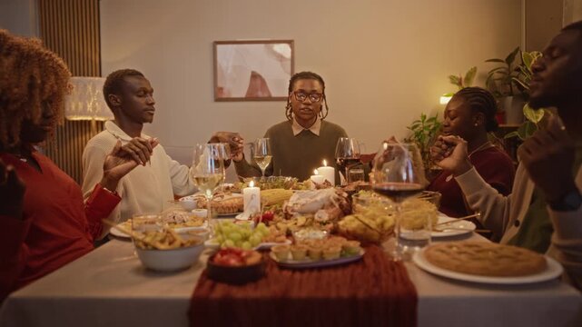 African American young adults holding hands and praying before festive Thanksgiving dinner. Clip suitable for autumn holiday marketing, diversity campaigns, and food commercials