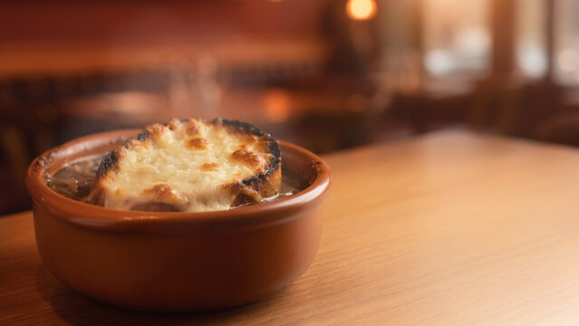 French onion soup with melted cheese in bowl with blurred bistro background banner.