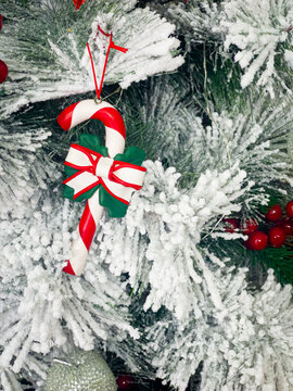 Candy cane Christmas ornament with red and white ribbon hanging on a snow covered tree. 