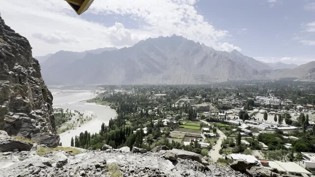 Elevated panoramic view of the Indus River flowing past Skardu City in Gilgit-Baltistan, Pakistan, with green urban areas, rocky terrain and dramatic rugged mountains