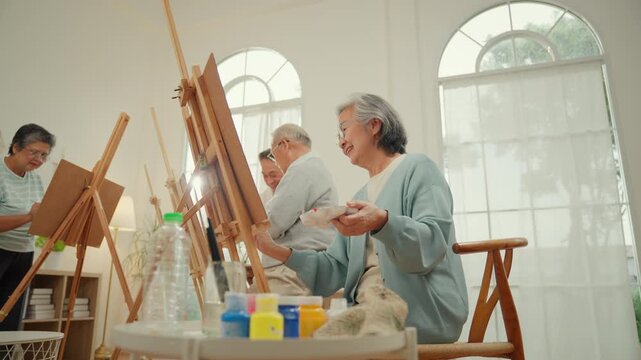 Happy senior elderly woman painting during an art therapy activity in a nursing home with caregiver support, promoting mental health, emotional wellbeing, creativity and active aging.