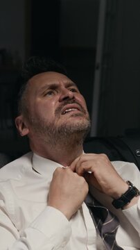 Vertical shot of middle aged Caucasian businessman struggling to unbutton collar and loosening tie. Clip fits mental health awareness campaigns and substance abuse treatment advertising