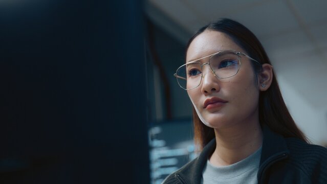 Clear glasses catch dim light as software aids a developer as an engineer reviews programming for coding, while software aids a developer as an engineer reviews programming for coding near a monitor.