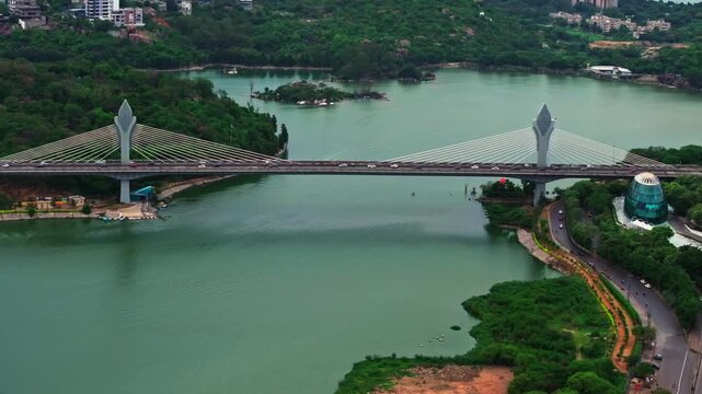 Vehicles moving on cable-stayed bridge with Durgam Cheruvu, green hills and iLabs Oval Office at madhapur, hyderabad, telangana, india. day time, push back shot, drone shot, 4k.