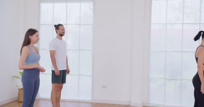 A diverse group of people learn proper posture and alignment from an instructor at the start of a yoga class in a bright, minimalist wellness studio, reflecting healthcare and preventive care themes.
