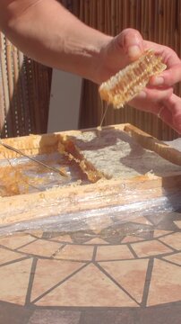 close-up of adult hands pressing, pulling, and separating sticky amber material from pale pulpy base inside shallow wooden tray on terracotta tile table, strong