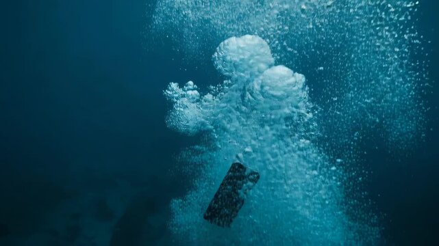 Phone falls into water creating bubbles and splashes in clear blue environment
