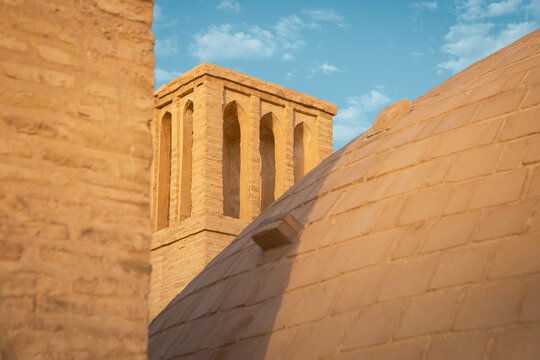Historic mud-brick dome and traditional windcatcher tower under a bright blue sky, showcasing classic Persian desert architecture and passive cooling systems in Iran.