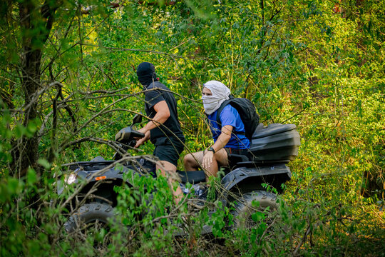 Riders on an ATV quad bike drive an off-road trail in a lush forest