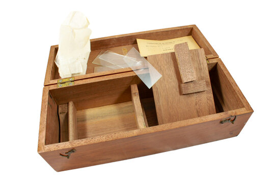 Wooden microscope storage case containing glass slides, a wooden slide holder, paper labels and protective tissue, isolated on a white background.