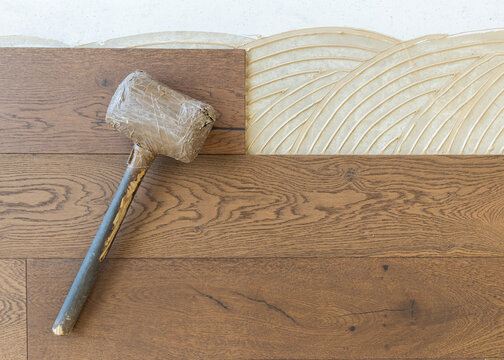 Rubber mallet on brown oak parquet planks during hardwood flooring installation, top view