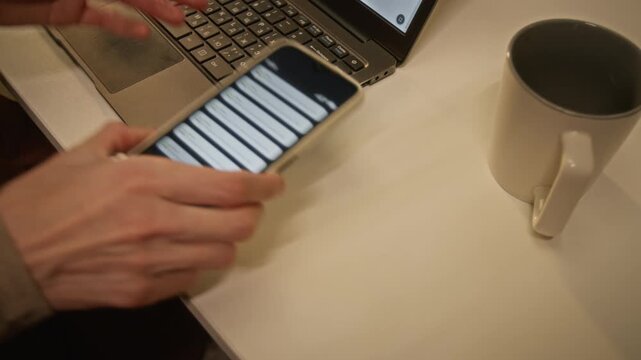 Unrecognizable adult typing on laptop keyboard, receiving push notifications and picking up smartphone. Suitable for technology projects about mobile alerts, remote work and digital communication