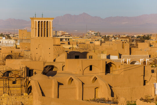 Traditional adobe houses around Narin Castle in Meybod, Iran. The historic earthen architecture of an arid desert settlement. A windcatcher against the backdrop of mountains and blue sky