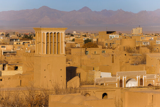 Traditional adobe houses around Narin Castle in Meybod, Iran. The historic earthen architecture of an arid desert settlement. A windcatcher against the backdrop of mountains
