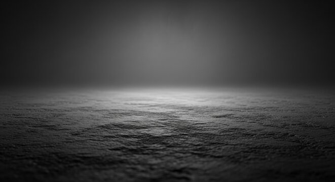 Monochromatic dark scene featuring a rough textured stone floor surface with soft glowing mist and hazy light fog in the background under dim cinematic lighting conditions.